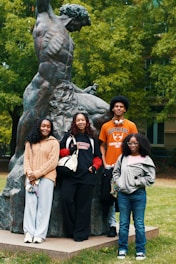 Four students pose for a photo near statue.