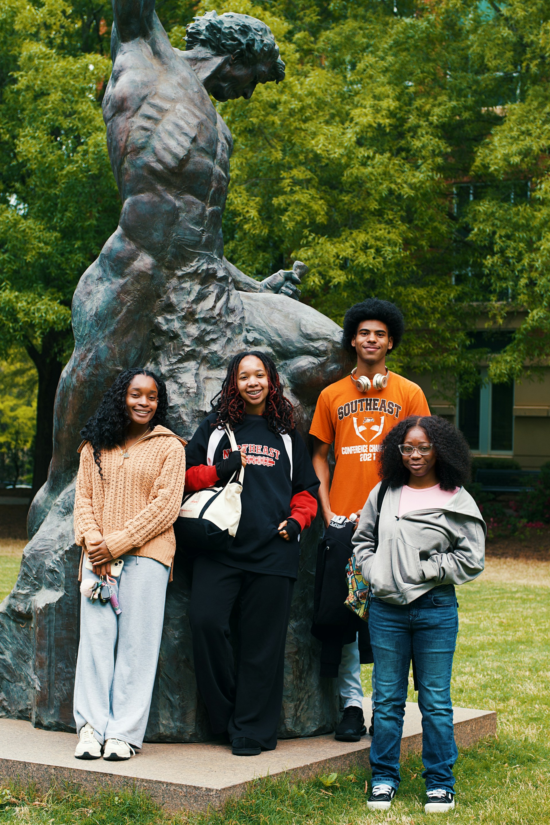 Four students pose for a photo near statue.