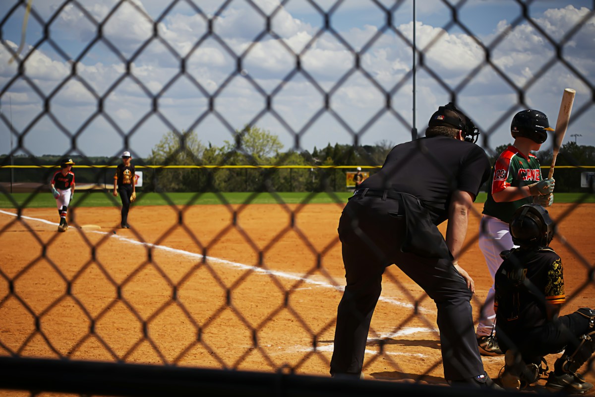 View of a baseball game through a chain link fence, players on the field, perfect for youth sports snack planning context