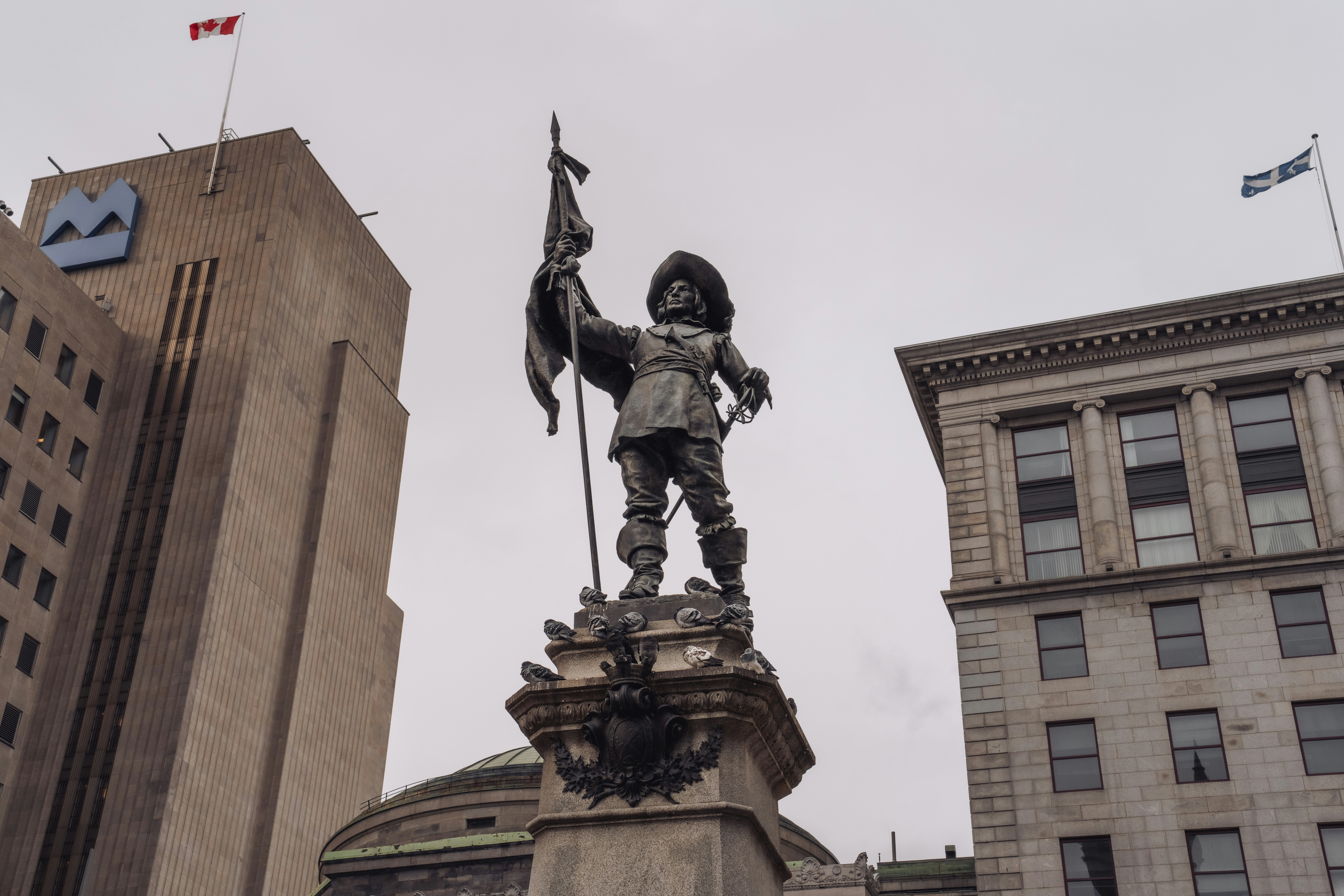 Montreal public square with Canadian and Quebec flags flying above heritage buildings