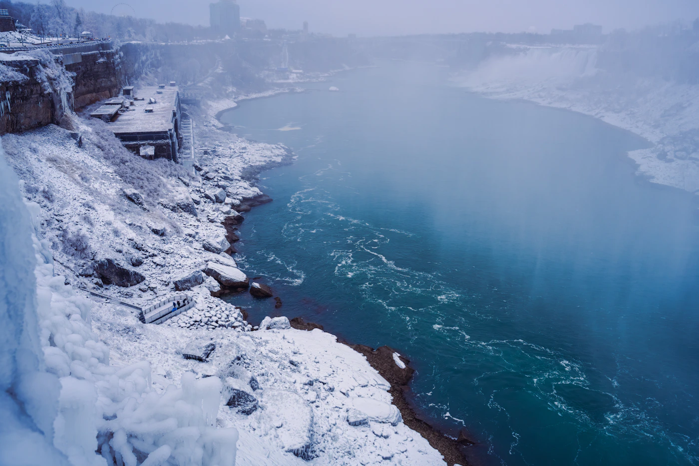 Niagara Falls in winter with turquoise blue frozen ice formations on the rocks and partially frozen water with the green-blue water still flowing through the ice formations under a winter sky