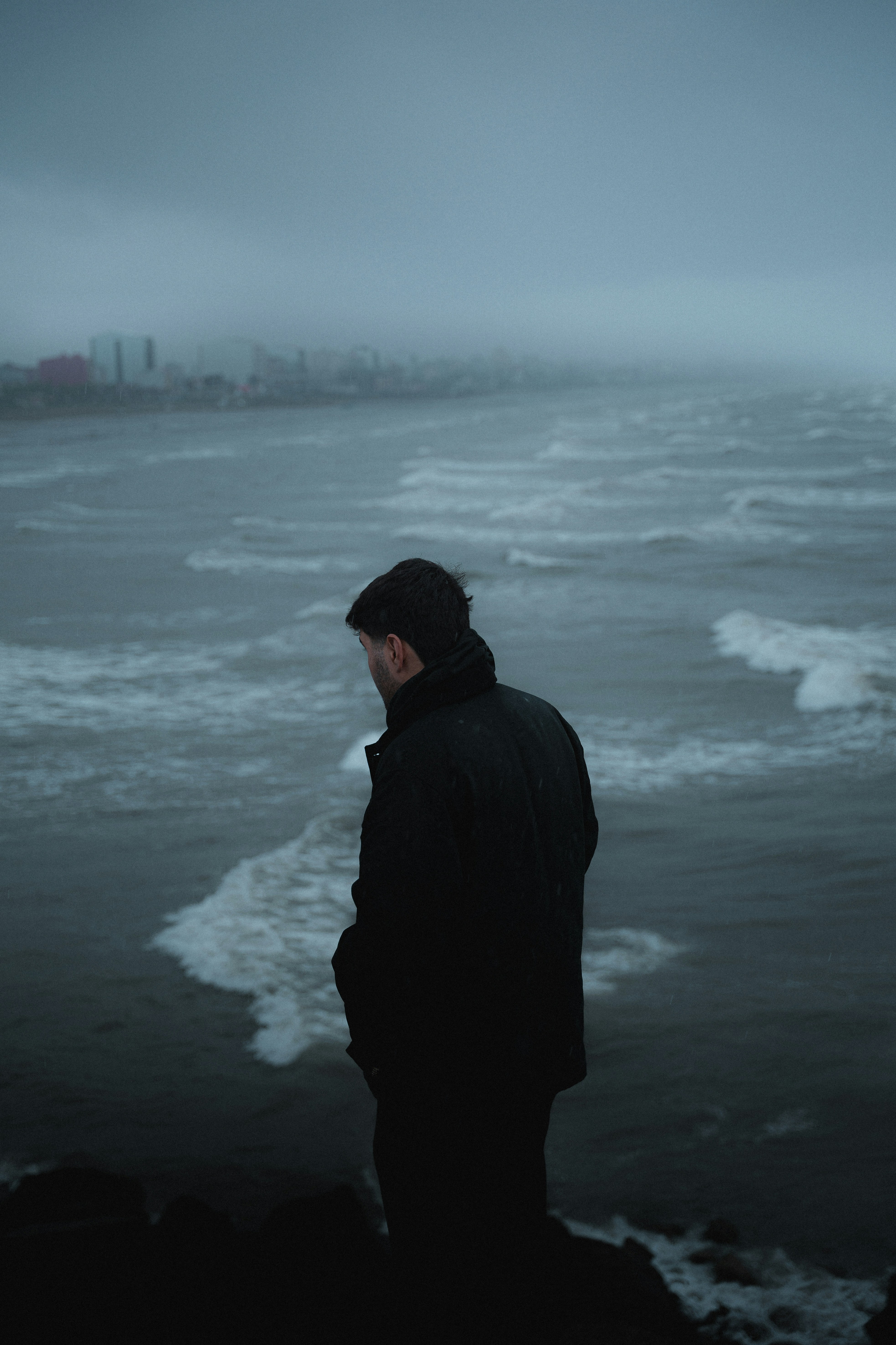 A man stares out at a misty, rough ocean.