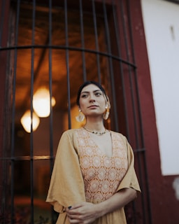 Woman in a dress poses by a barred window.