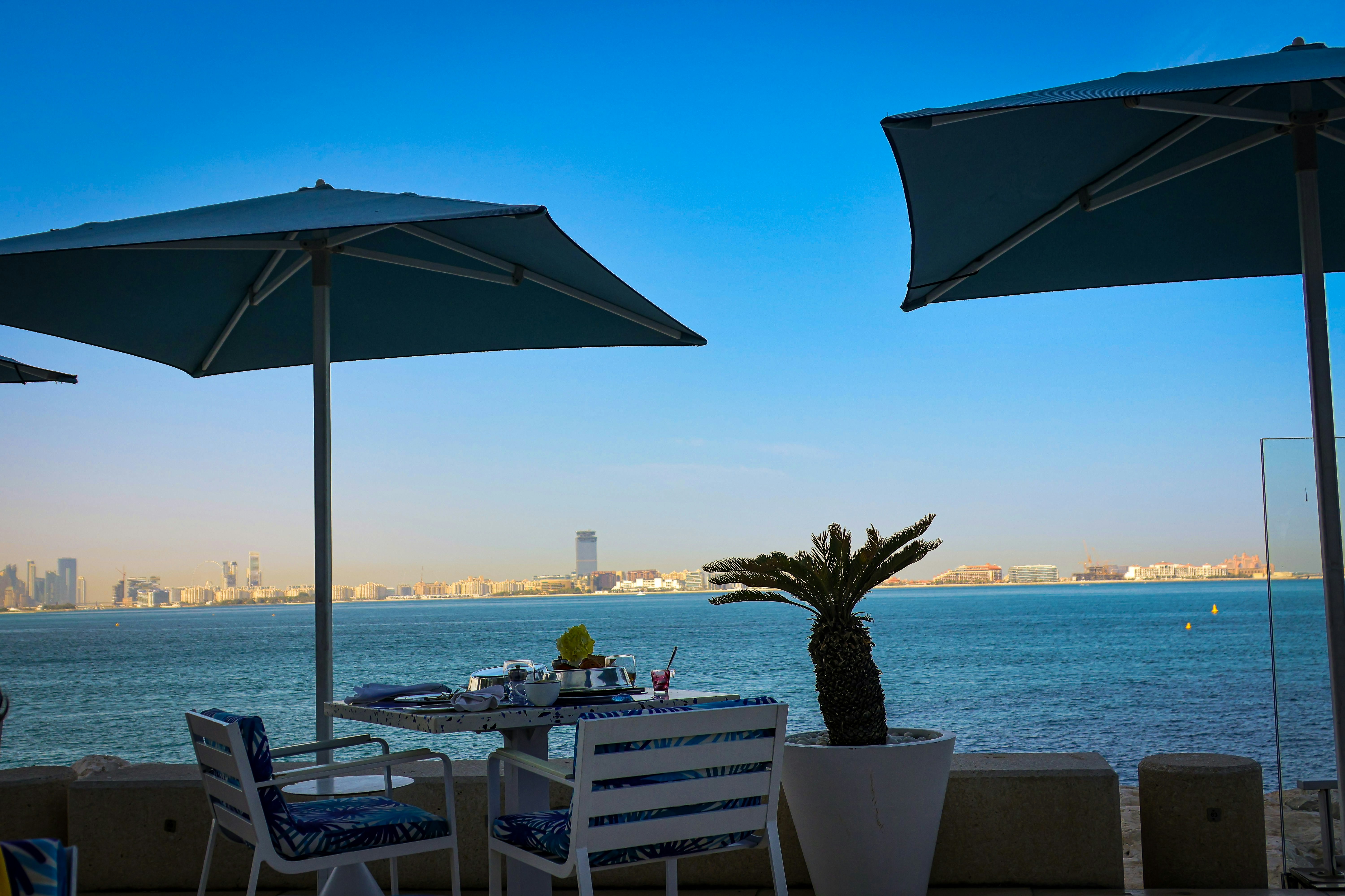 Restaurant tables overlook the ocean with umbrellas.