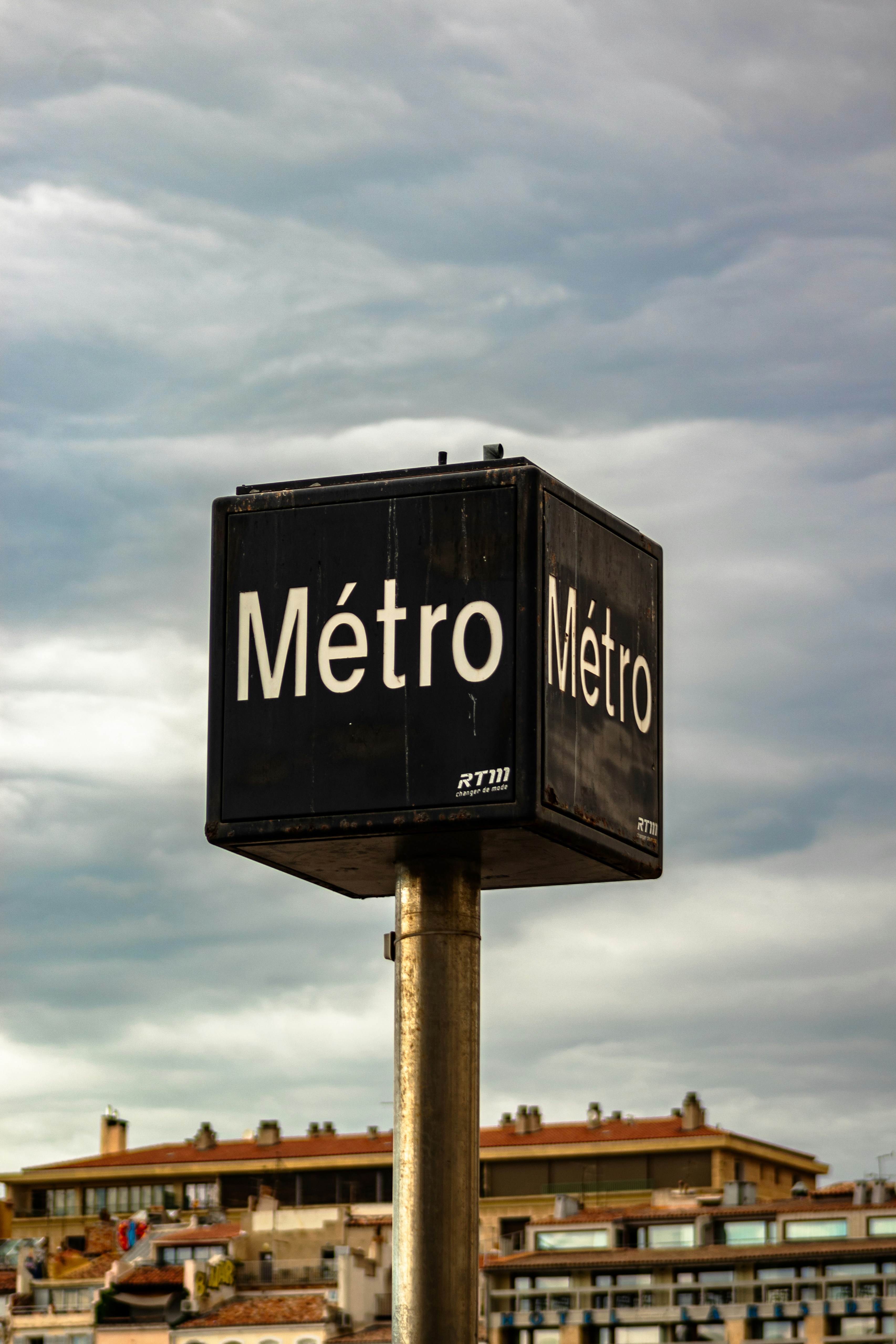 Metro station sign against a cloudy sky.
