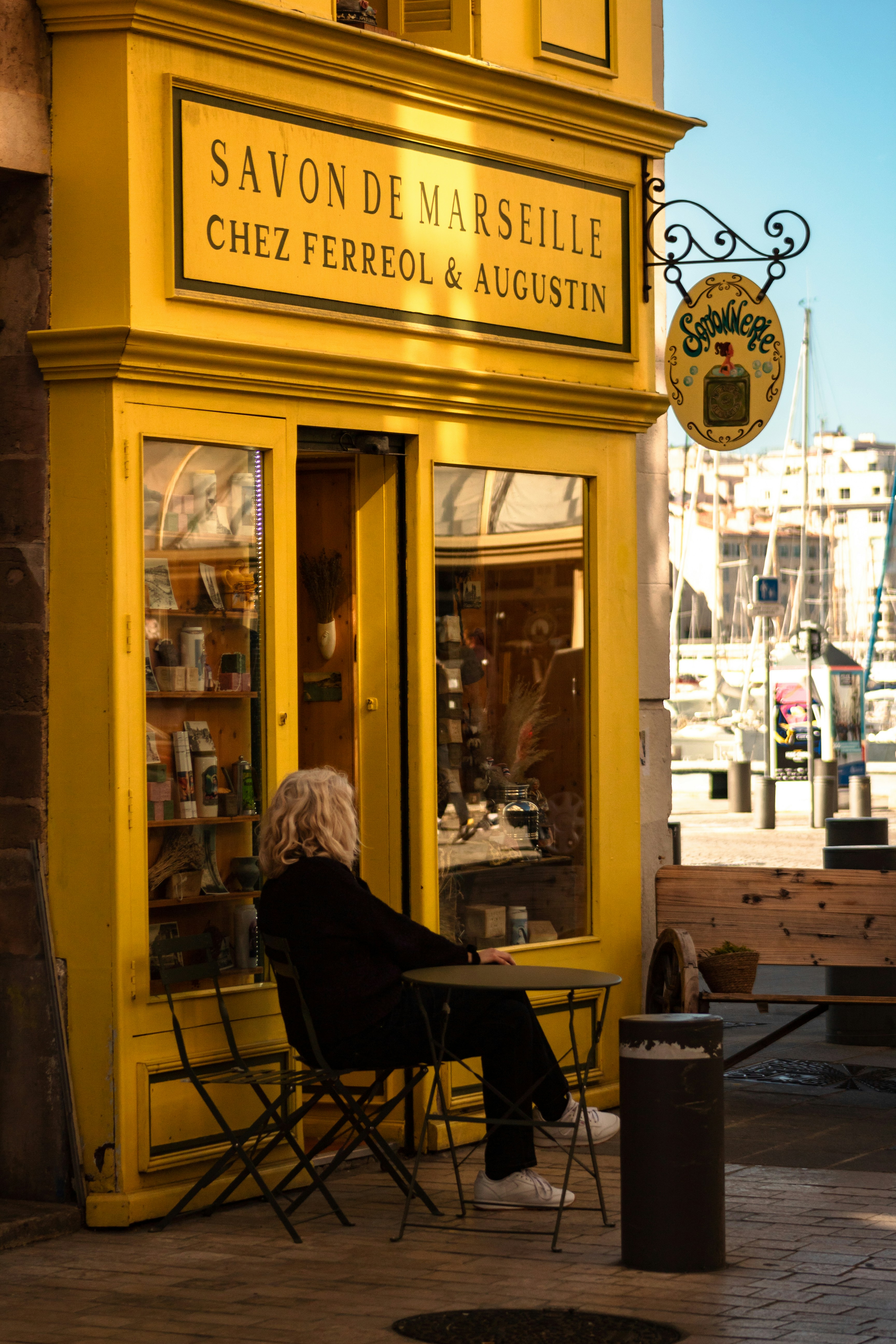 Woman sits outside a yellow shop in marseille.