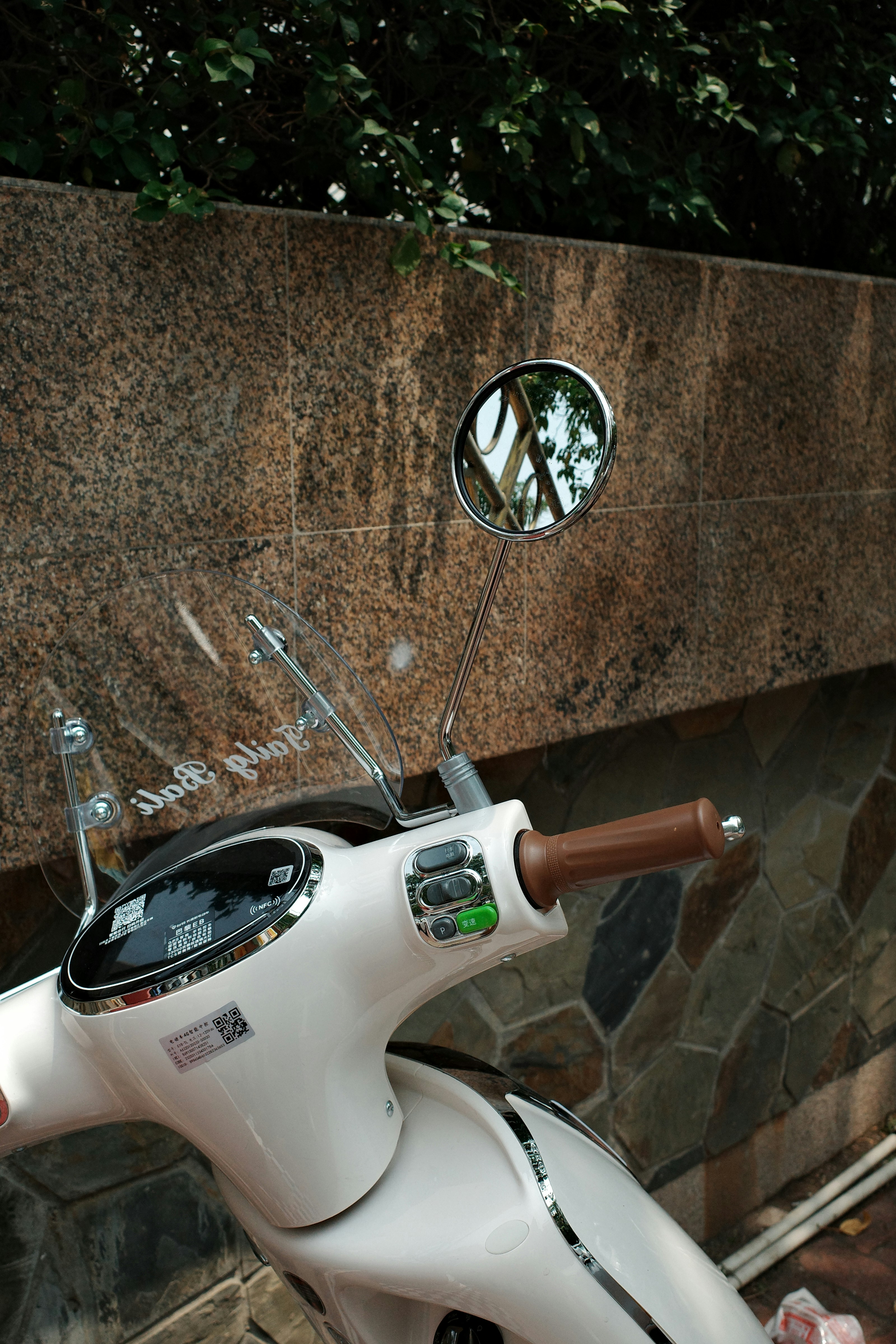 A white scooter is parked near a stone wall.