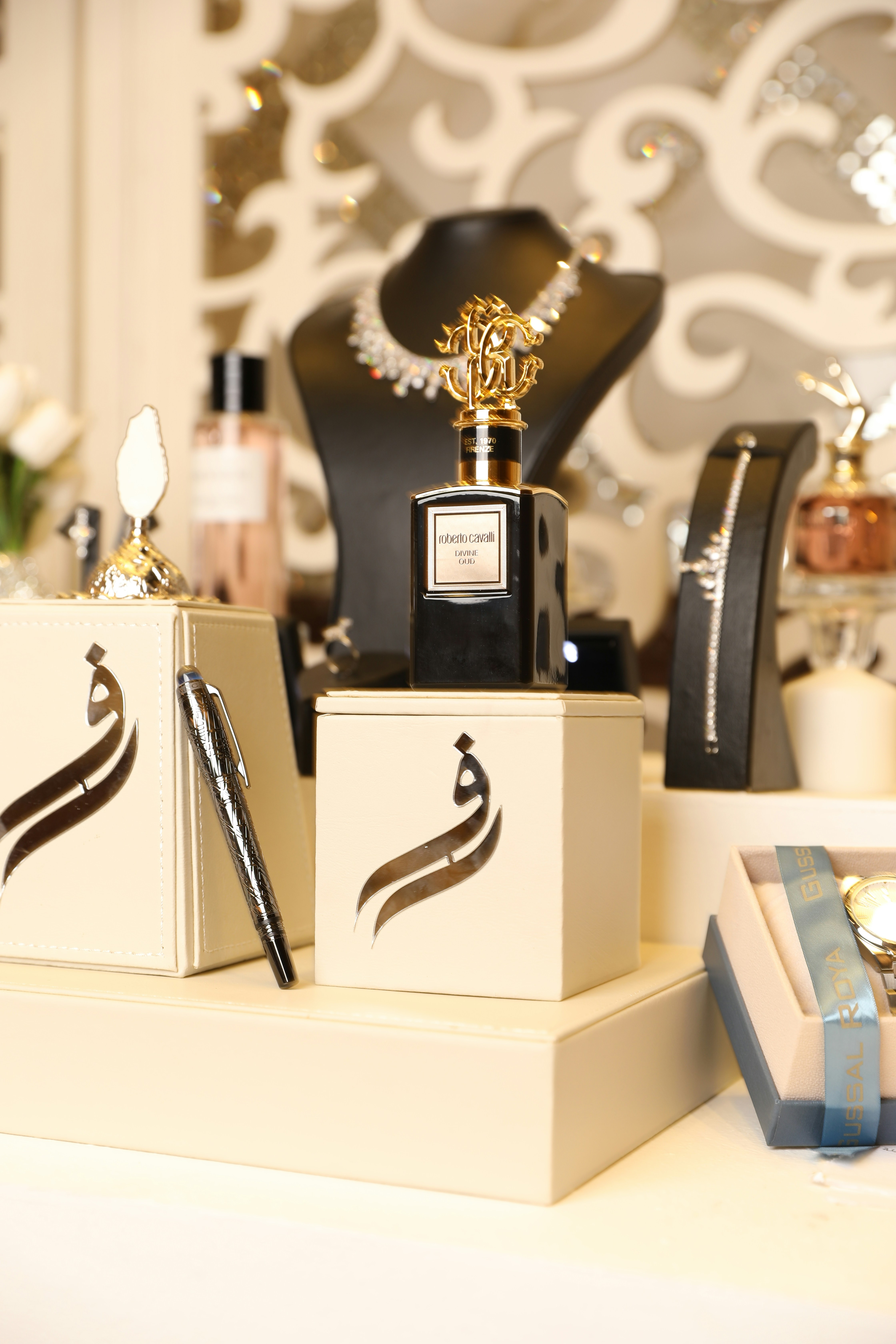 Luxury perfume, diamond necklace, and pen on display.