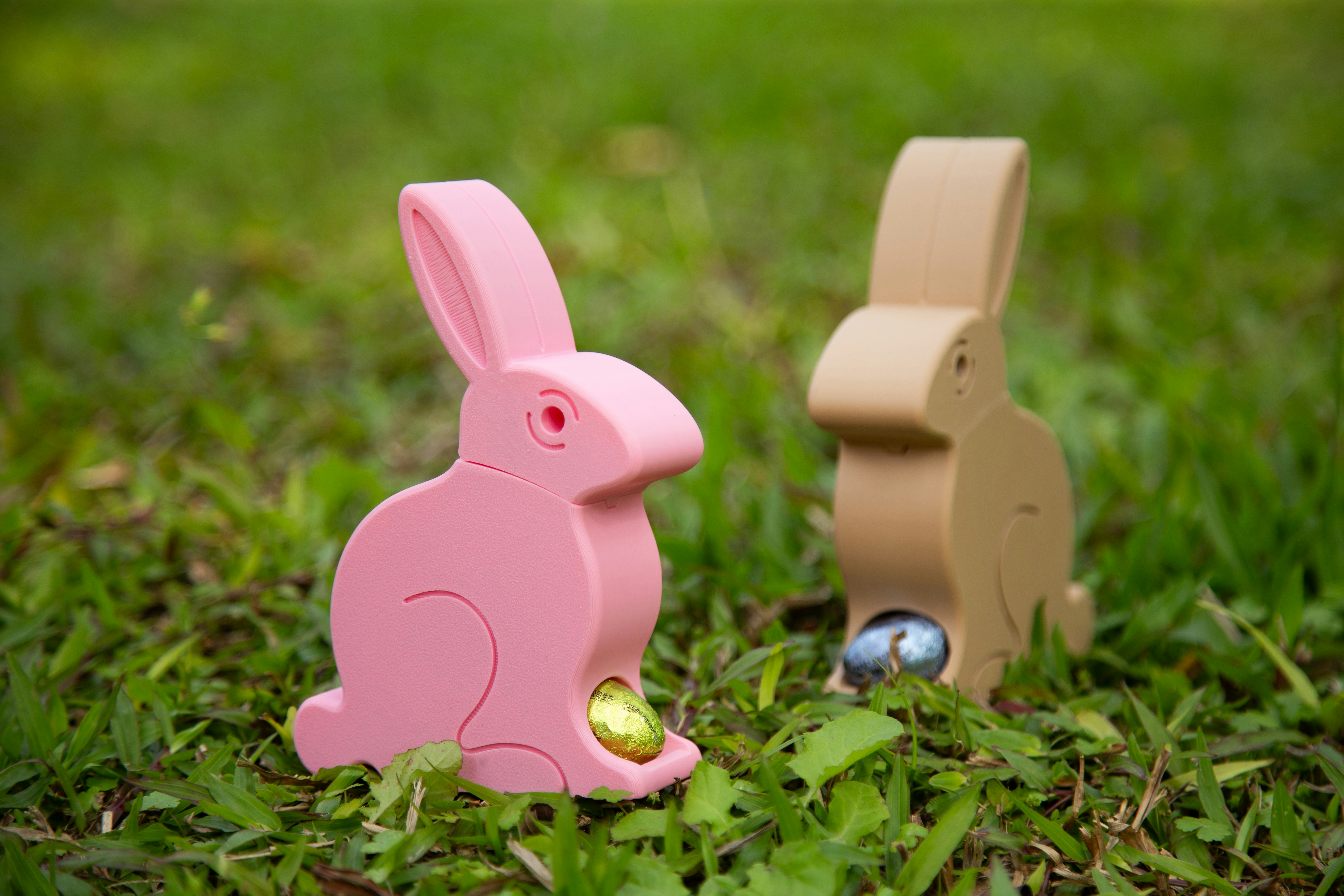Colorful 3D-printed bunnies in pastel pink and beige, each holding an Easter egg.