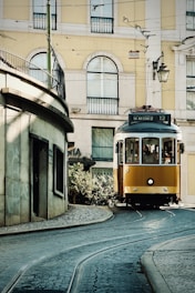 A yellow tram travels down a cobblestone street.