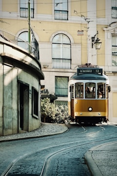 A yellow tram travels down a cobblestone street.