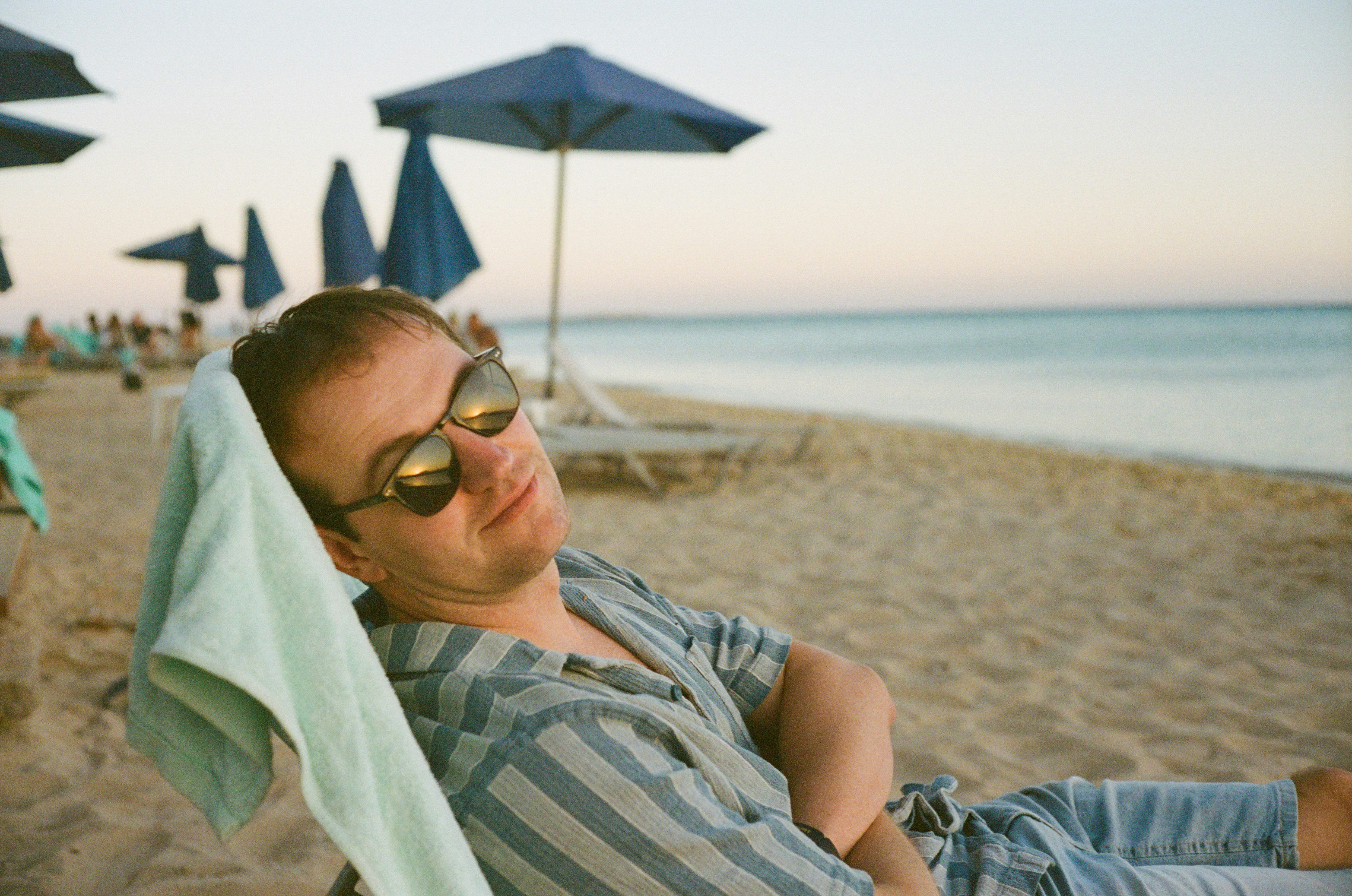Man relaxes on a beach with his sunglasses.