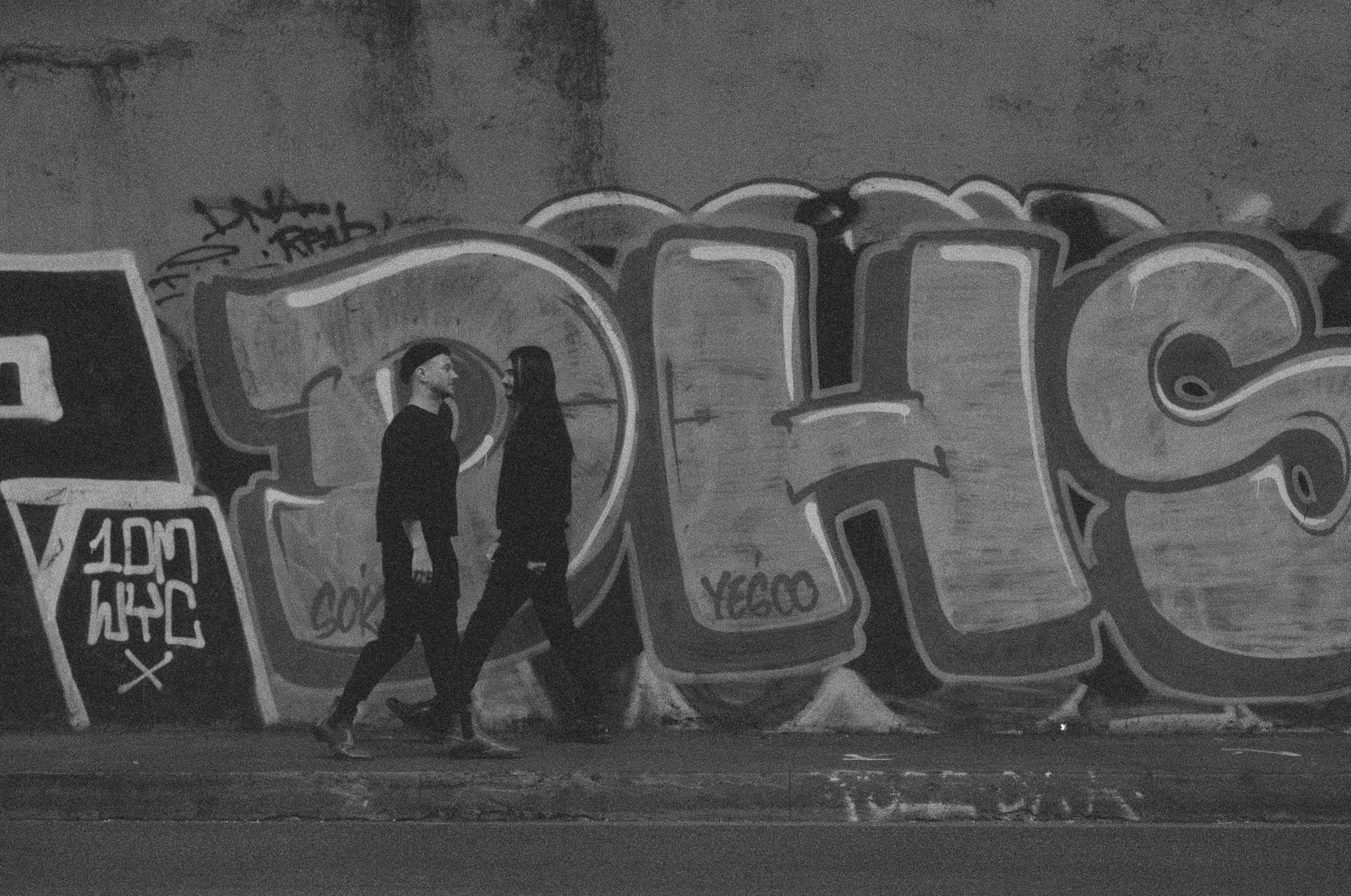 Two figures walk past graffiti on a wall.