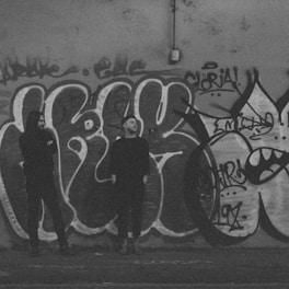 Two people stand in front of graffiti.