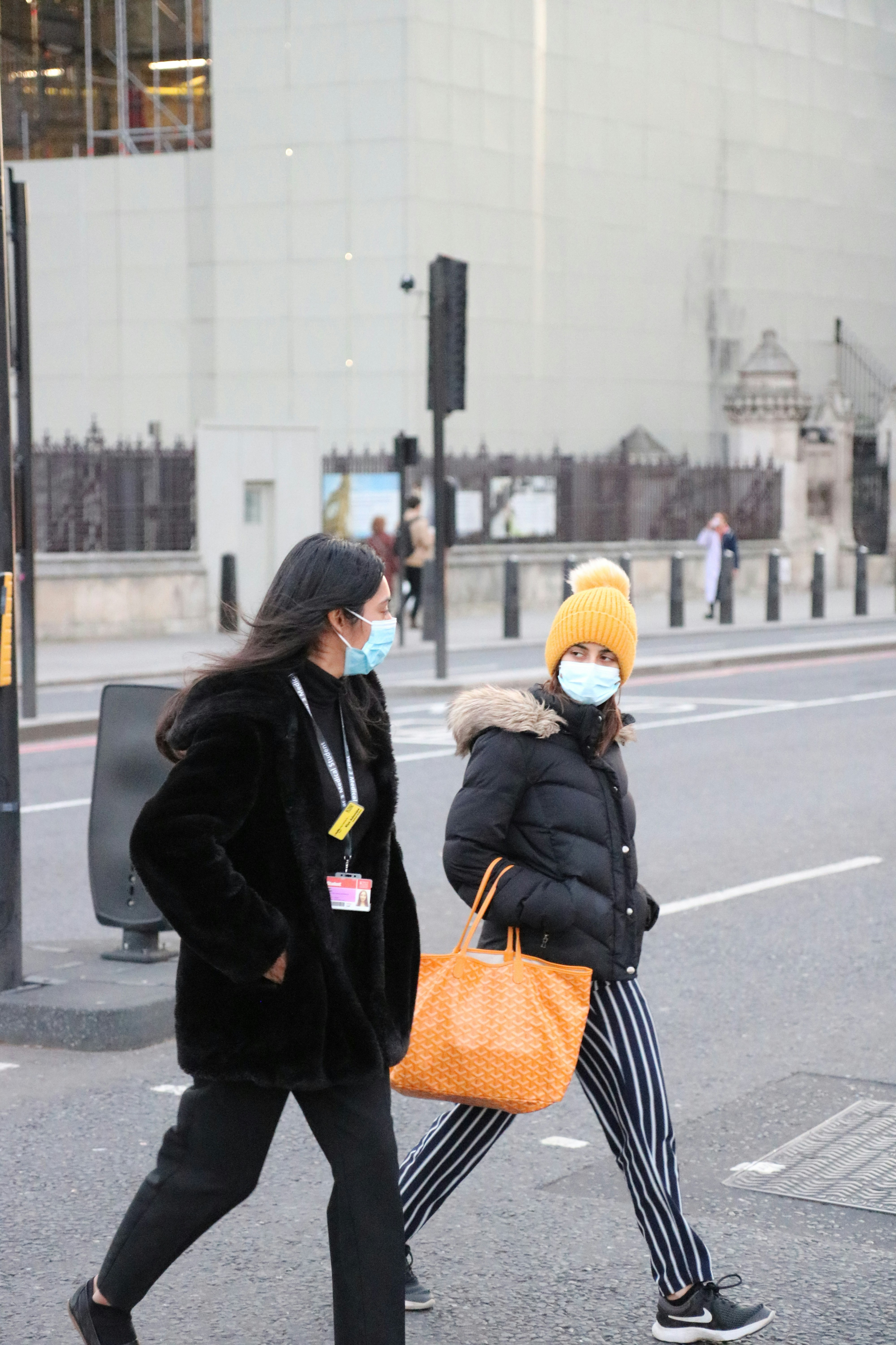 Two masked women walk across a crosswalk.