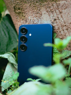 A blue smartphone rests against a tree