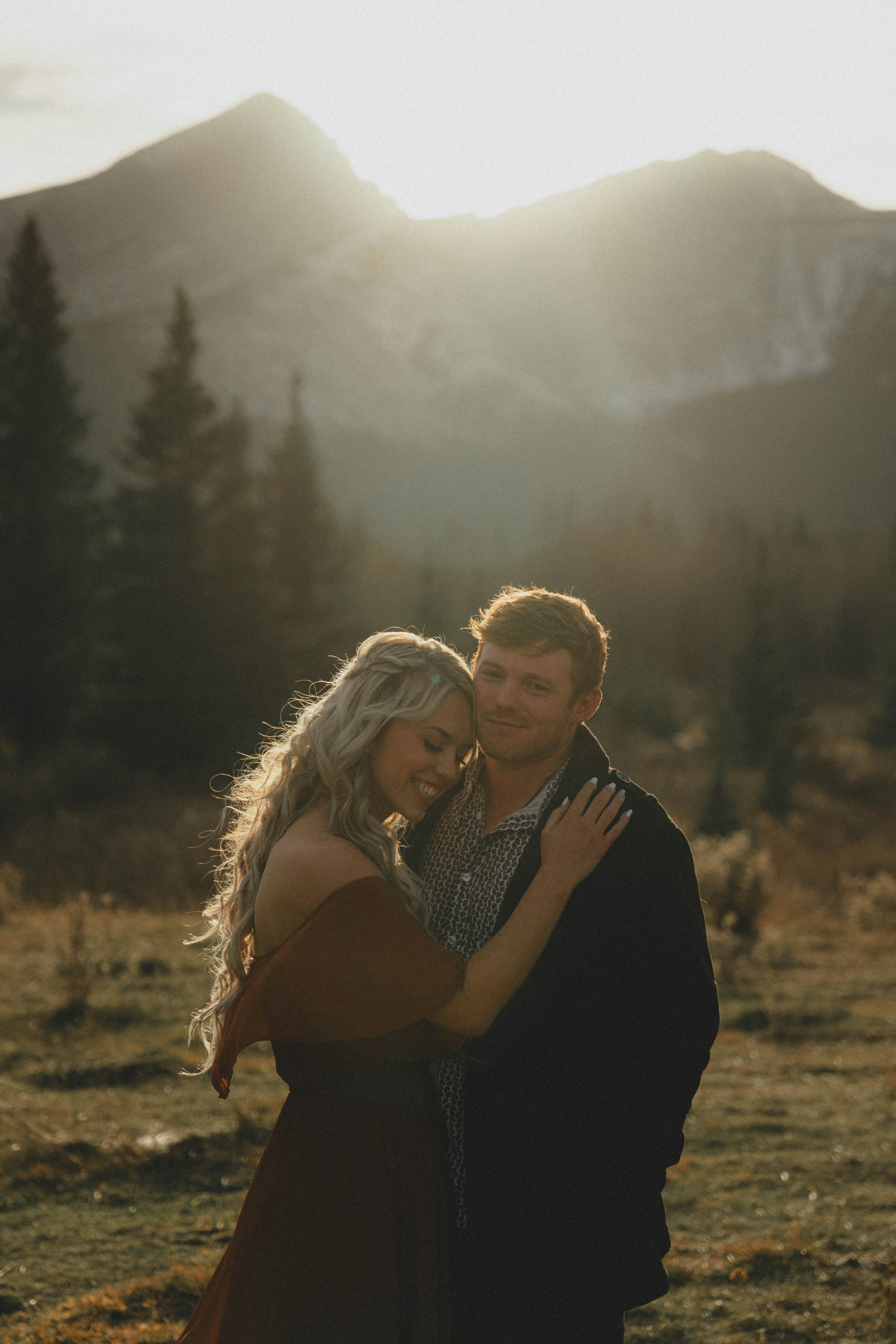 A smiling couple embraces in a mountainous landscape