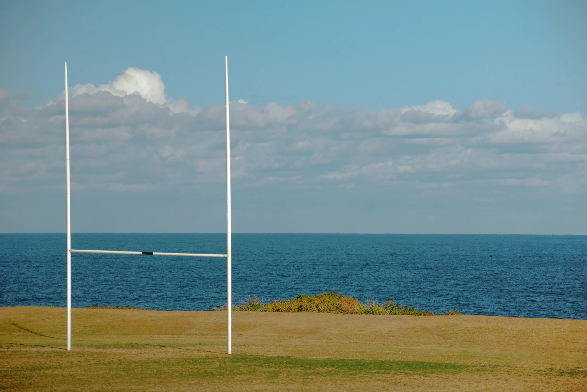 Rugby posts stand before the calm sea.