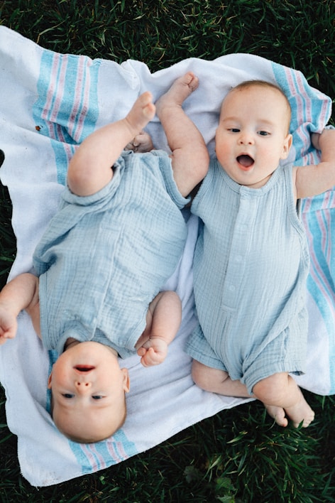 Two adorable babies are laying on a blanket.