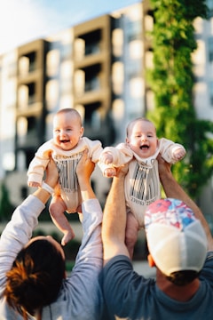 Parents happily lift adorable twin babies.