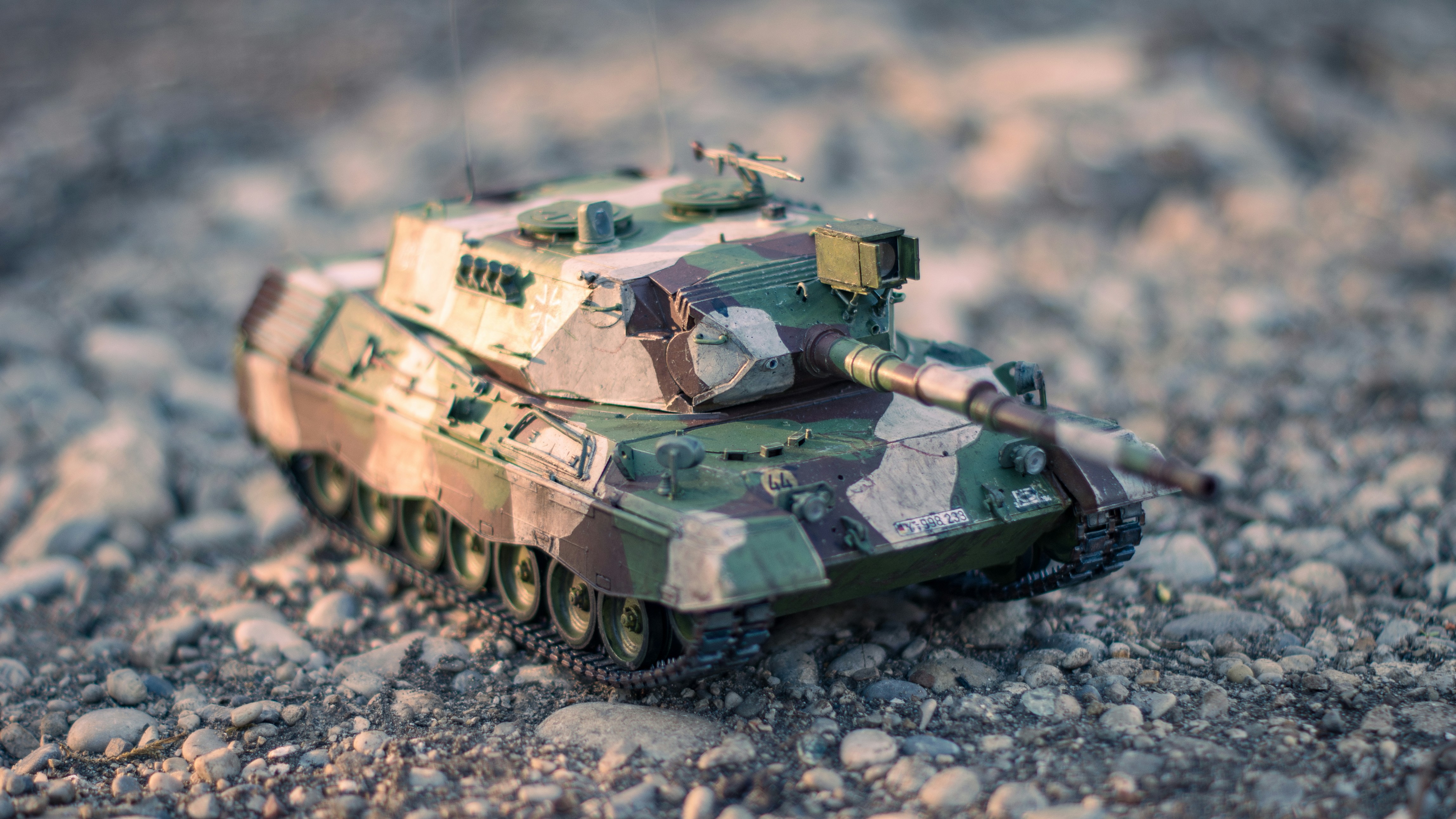 A small camouflaged tank sits on rocks.
