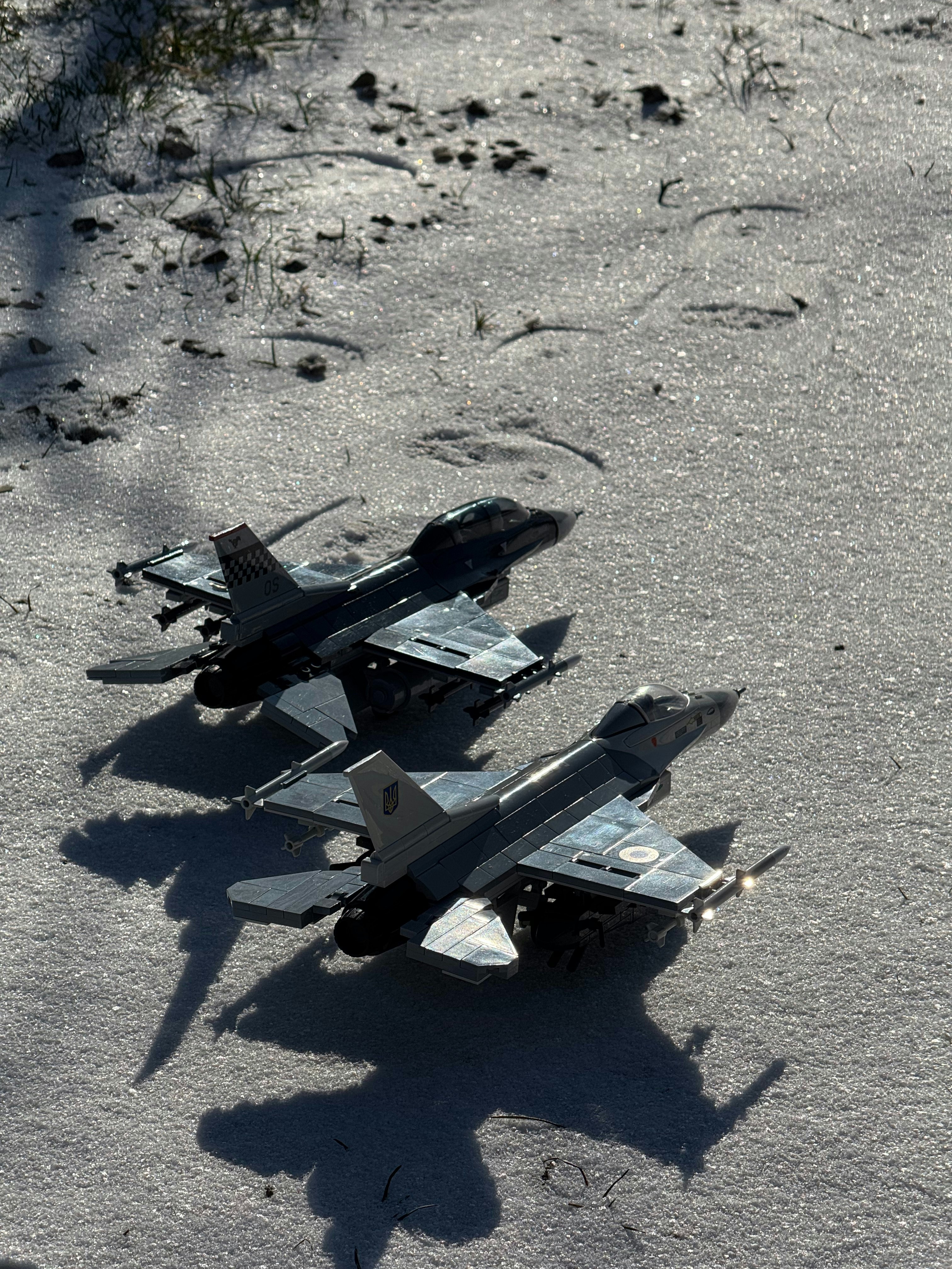 Toy fighter jets rest on a sandy surface.