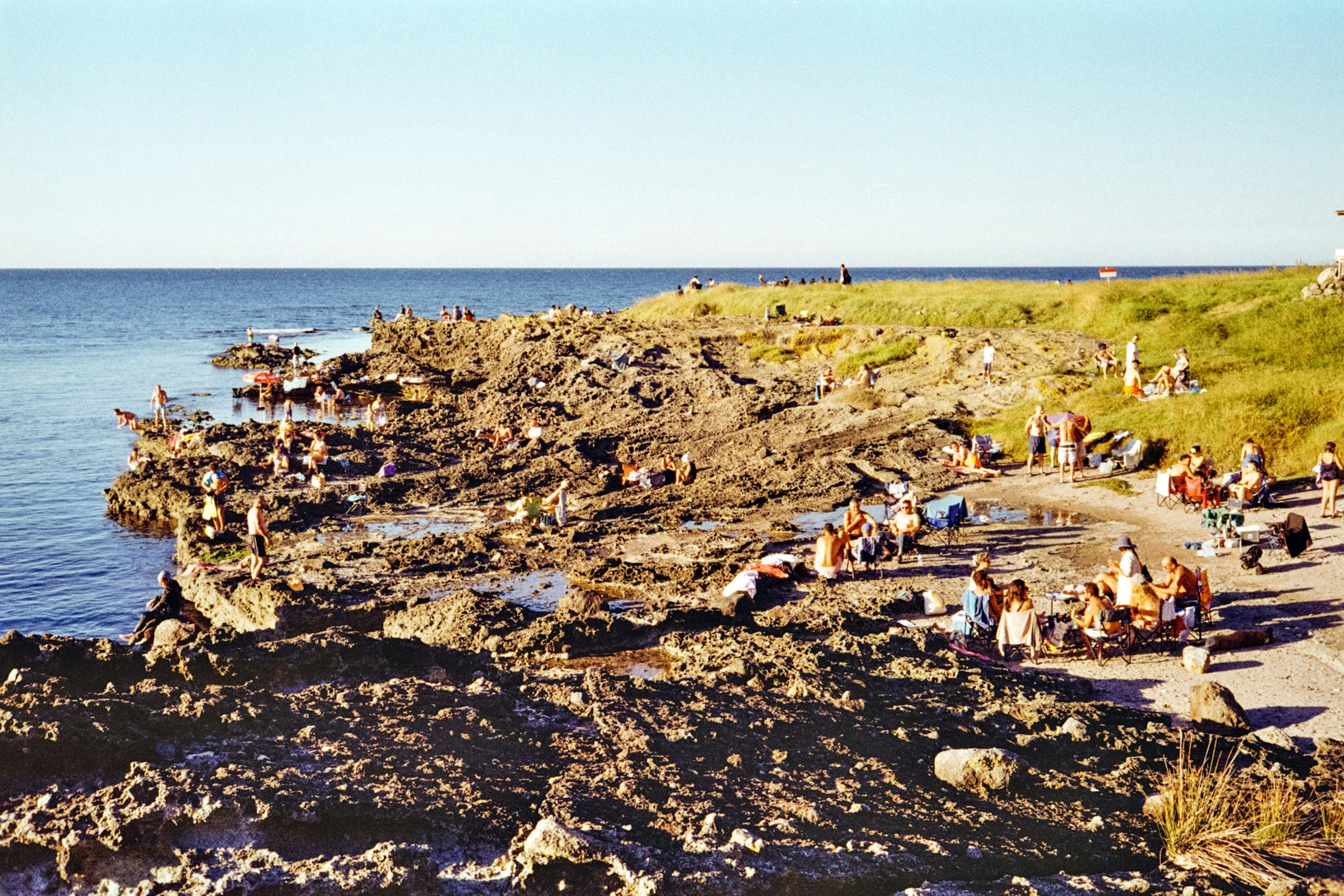 People enjoy swimming and relaxing along a rocky coastline.