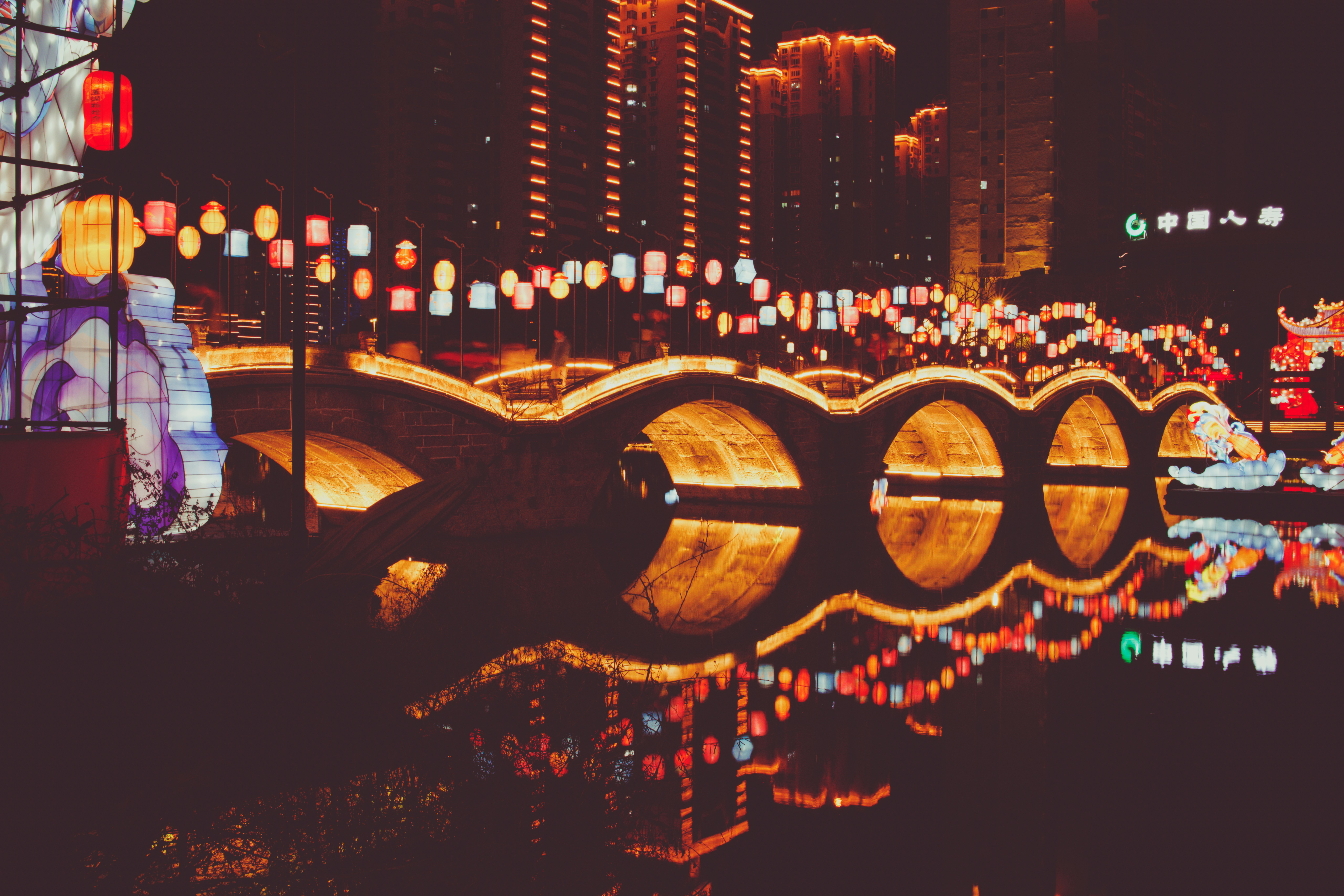 Nighttime bridge illuminated with lanterns and reflections.