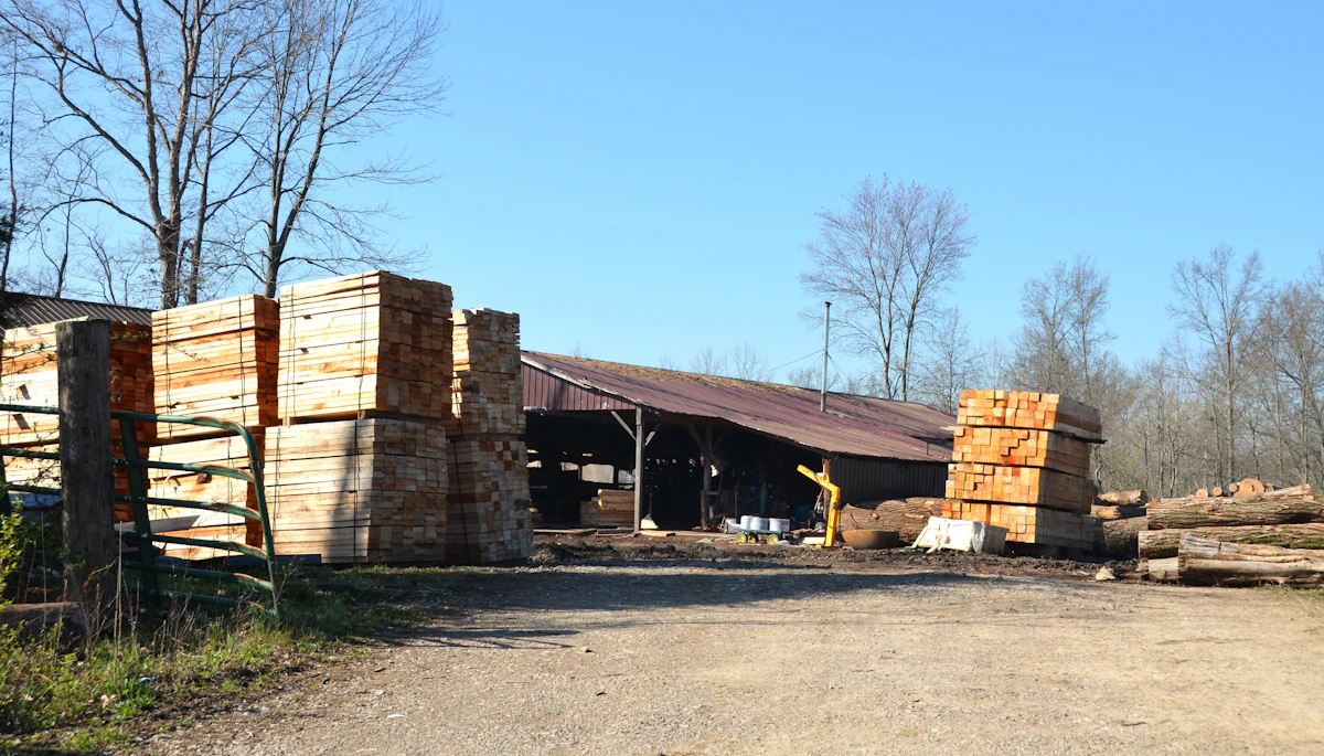 Lumber stacked at a materials yard beside a workshop shed