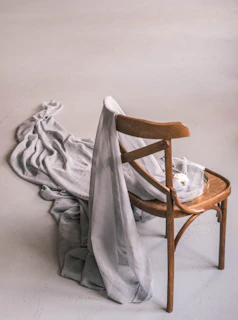 A wooden chair draped with gray fabric.
