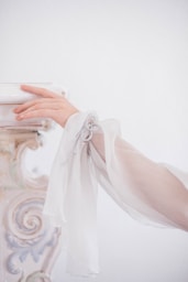 Elegant hand rests against a decorative white surface.