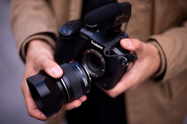 Hands hold a camera with a lens.
