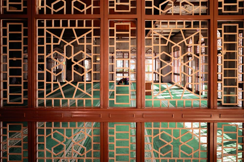 Ornate mosque interior with intricate wooden screens and arches, sunlight streaming through.
