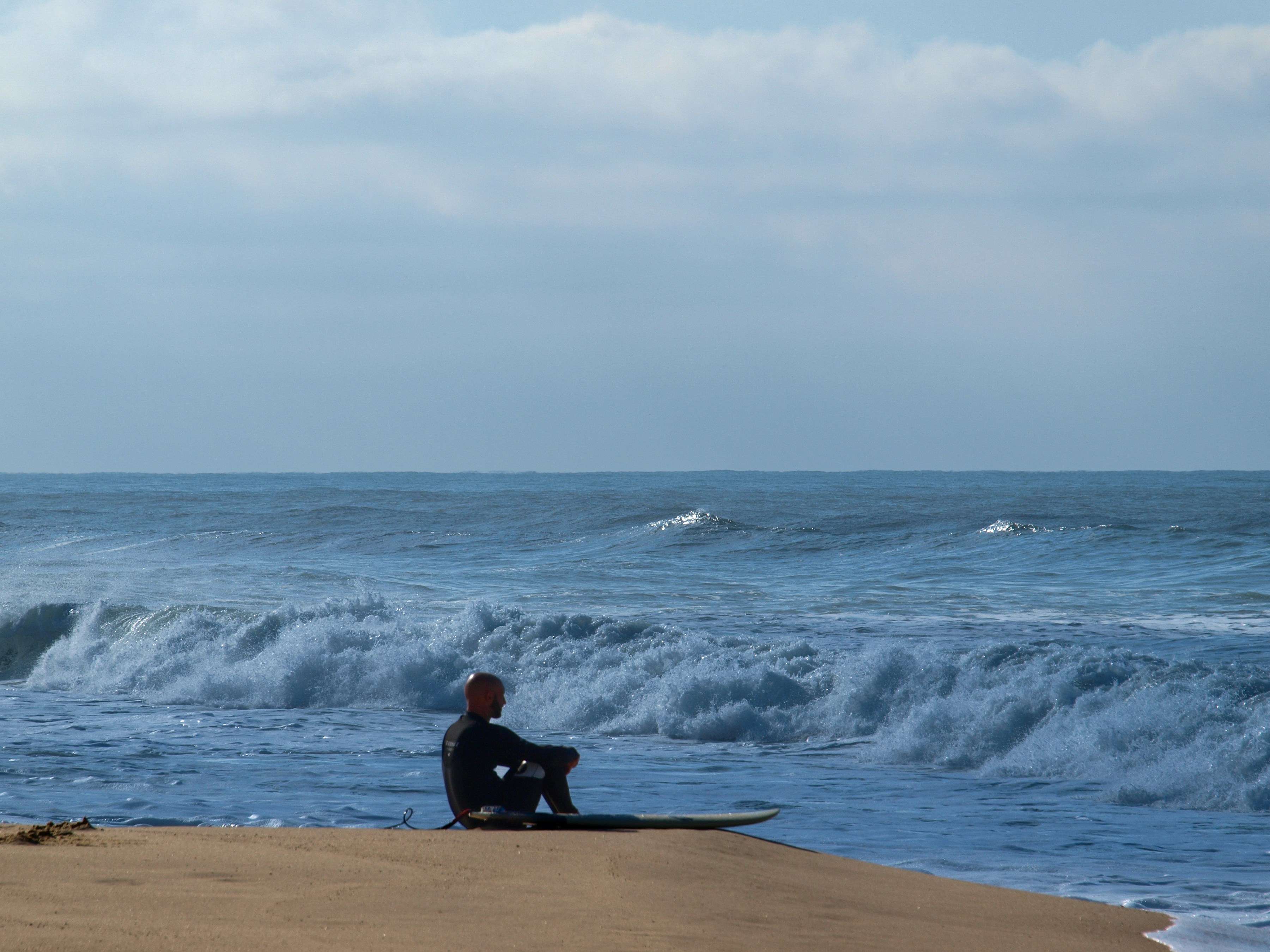 A surfer sits on a beach, contemplating the waves