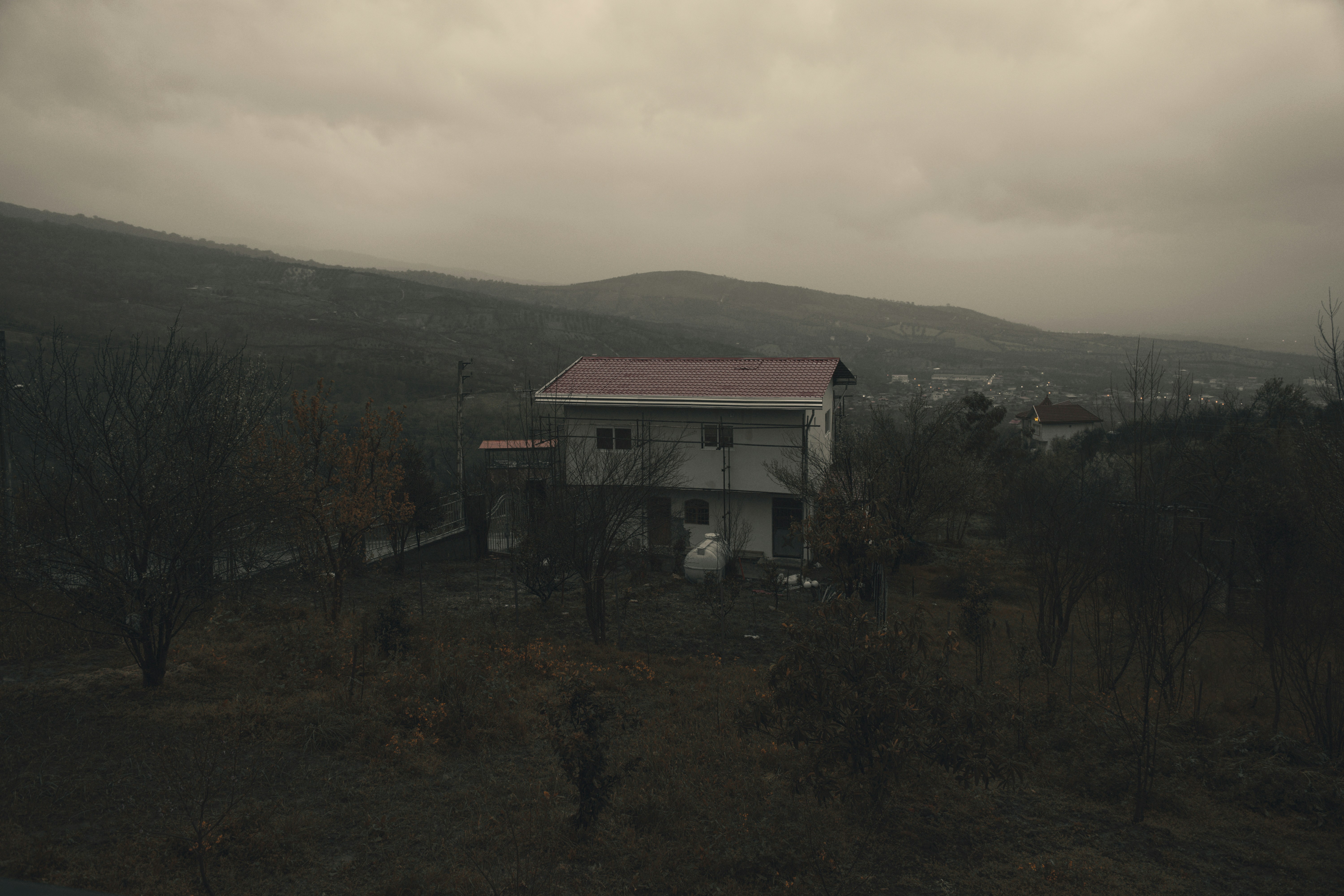 A house sits in a dreary, mountainous landscape.