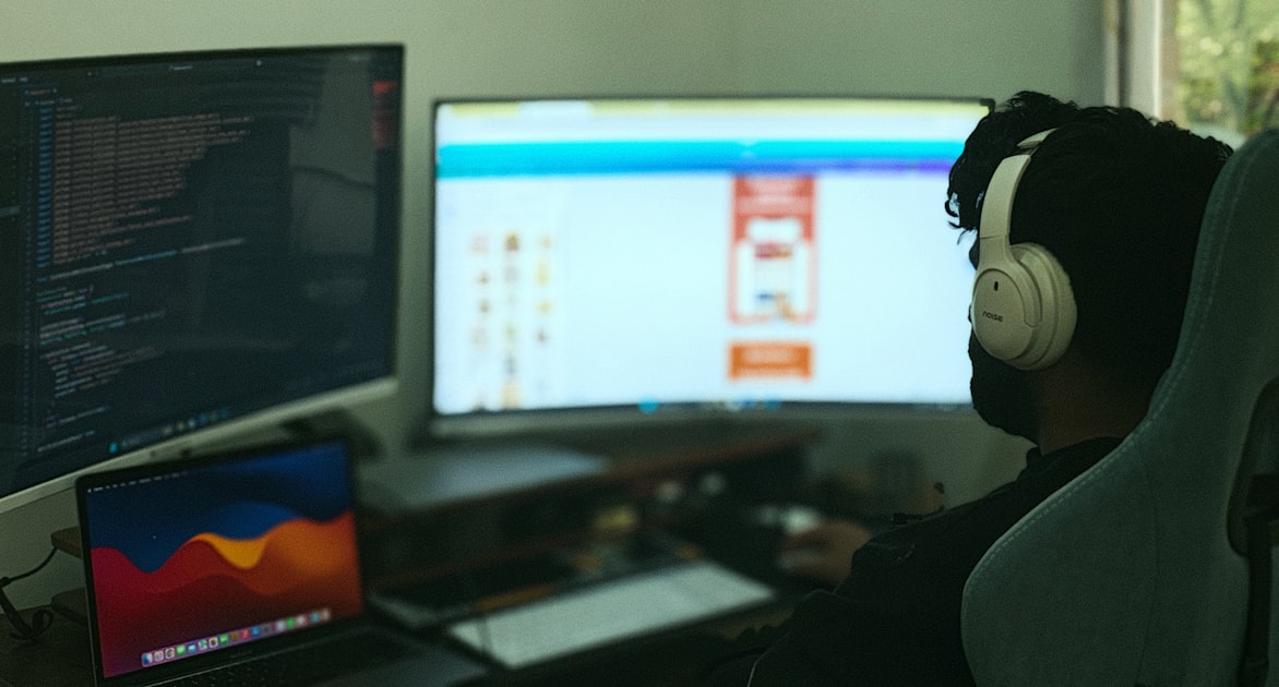 A developer at a multi-monitor coding setup with terminal windows and editors open — the daily-driver question that this article tries to settle