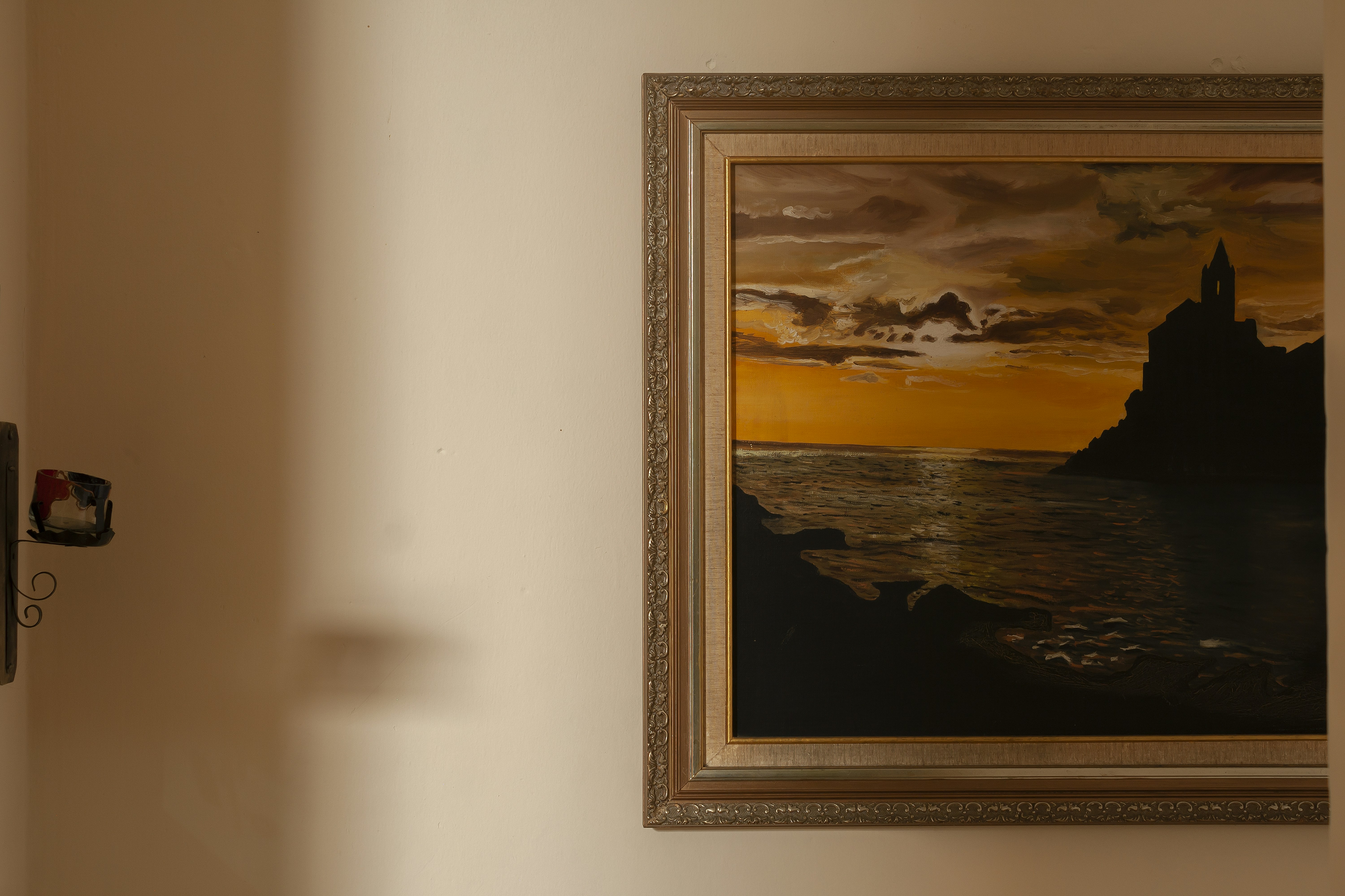 Una pintura enmarcada representa una puesta de sol sobre el agua.