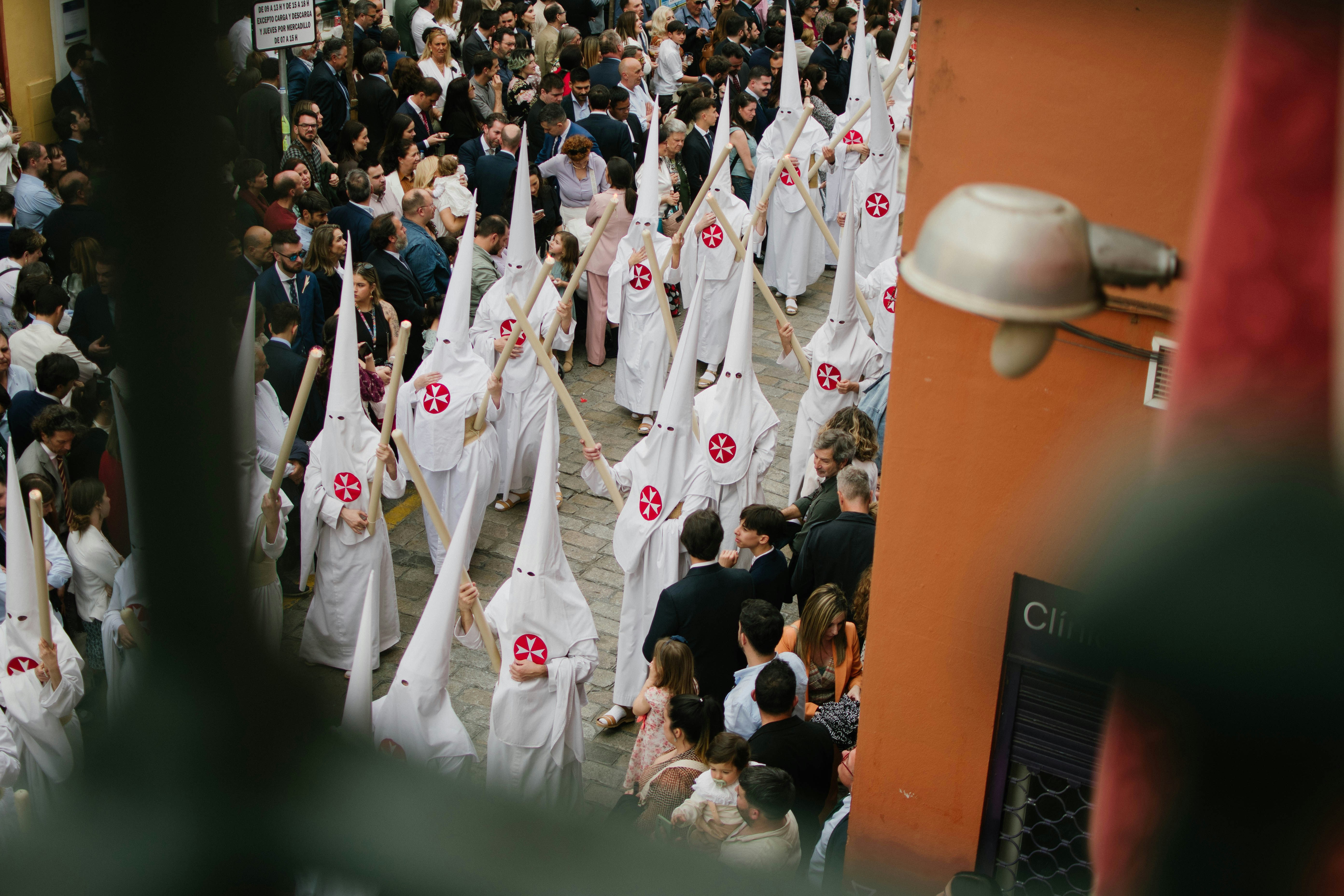 White-robed nazarenos with pointed hoods process through a Seville street during Semana Santa