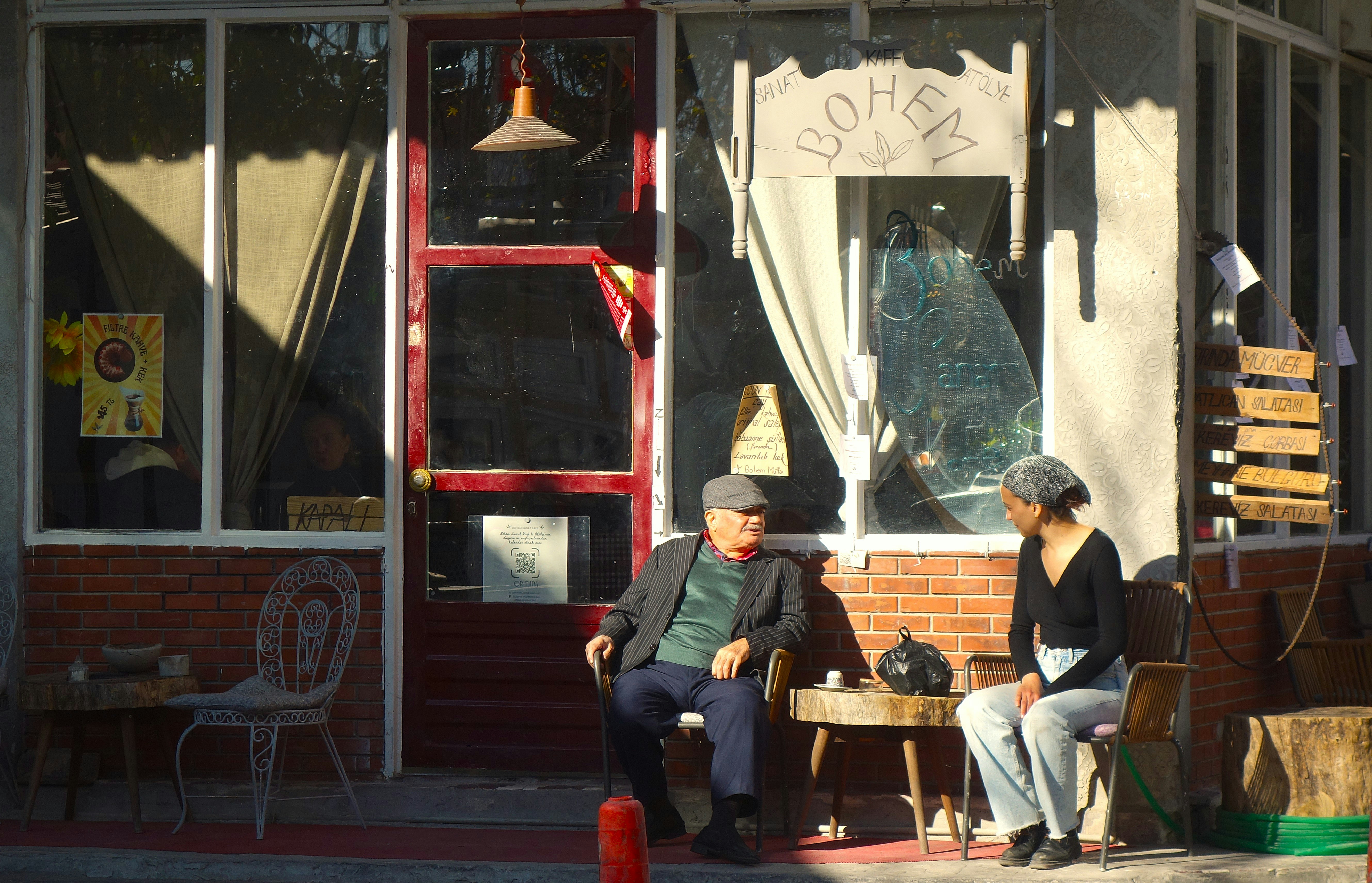 Two people are sitting outside a small shop.