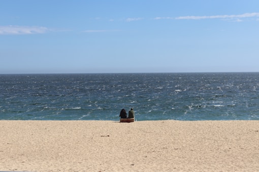 Couple sits on the beach, gazing at the ocean.