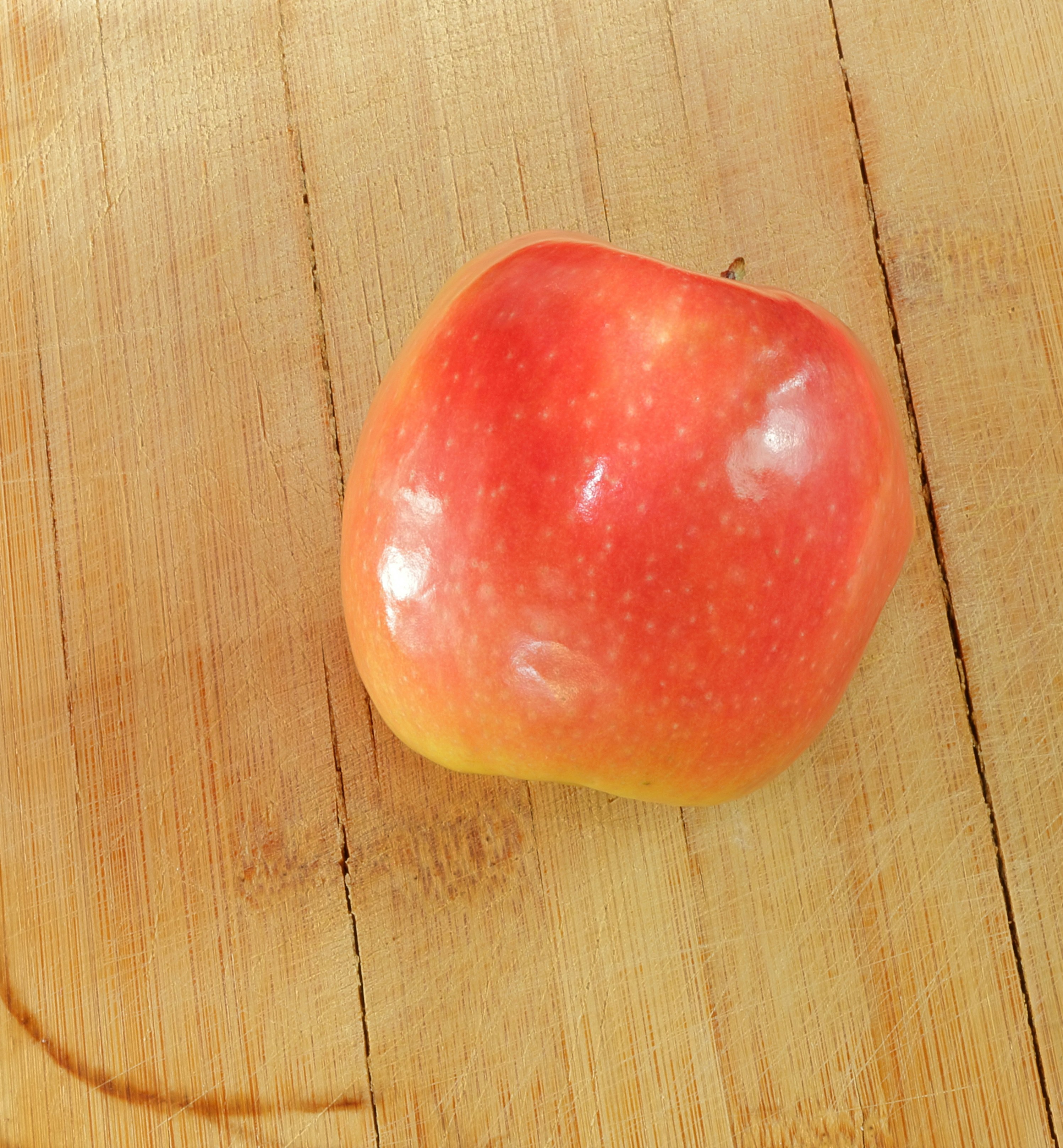 A red apple sits on wooden surface.