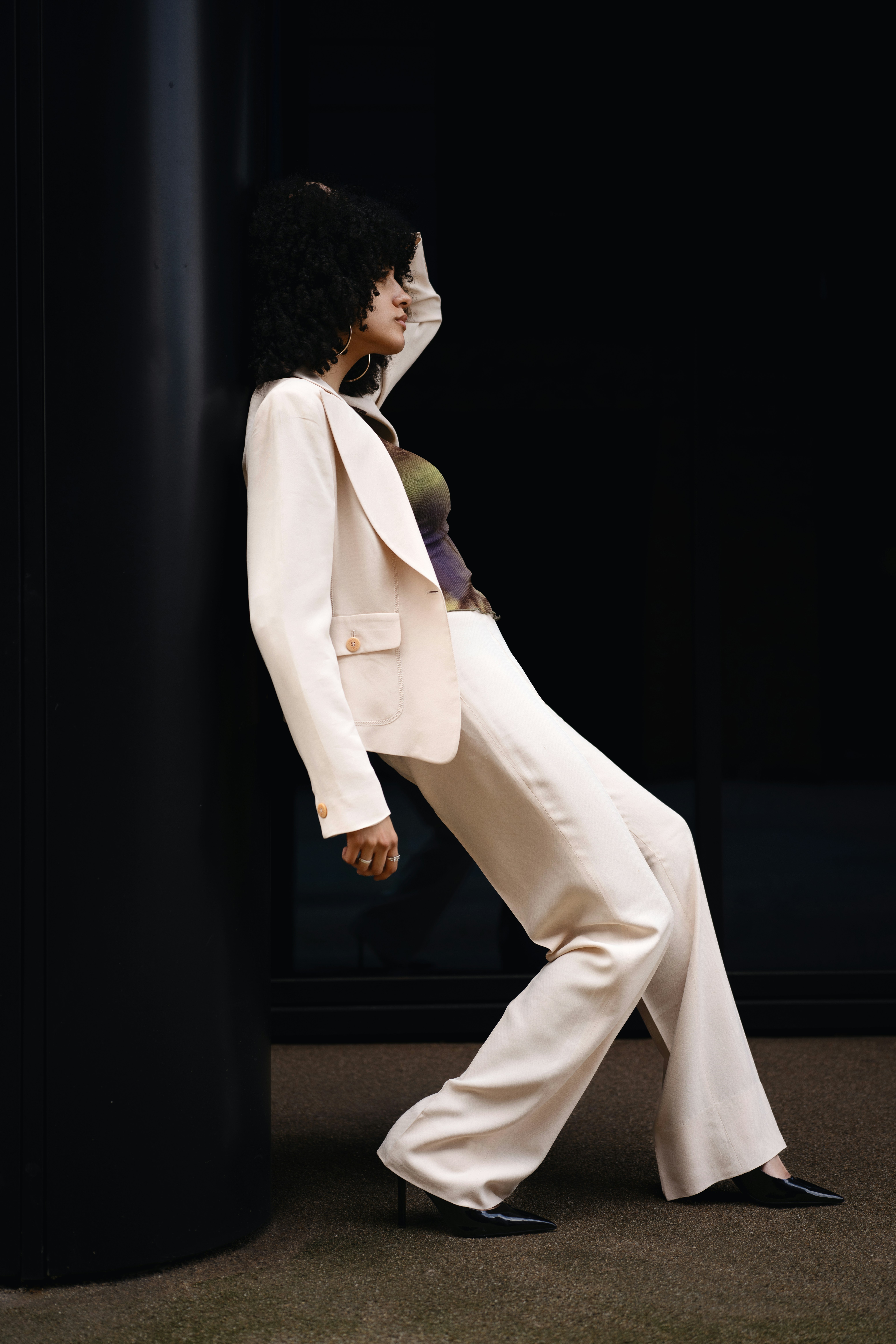 Woman leans against a black pillar, striking a pose.