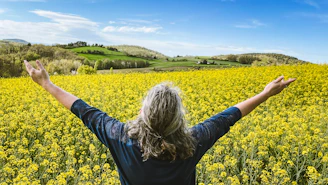 Woman embraces a field of yellow flowers.