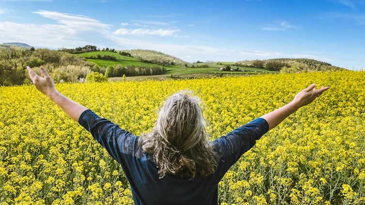 Woman embraces a field of yellow flowers.