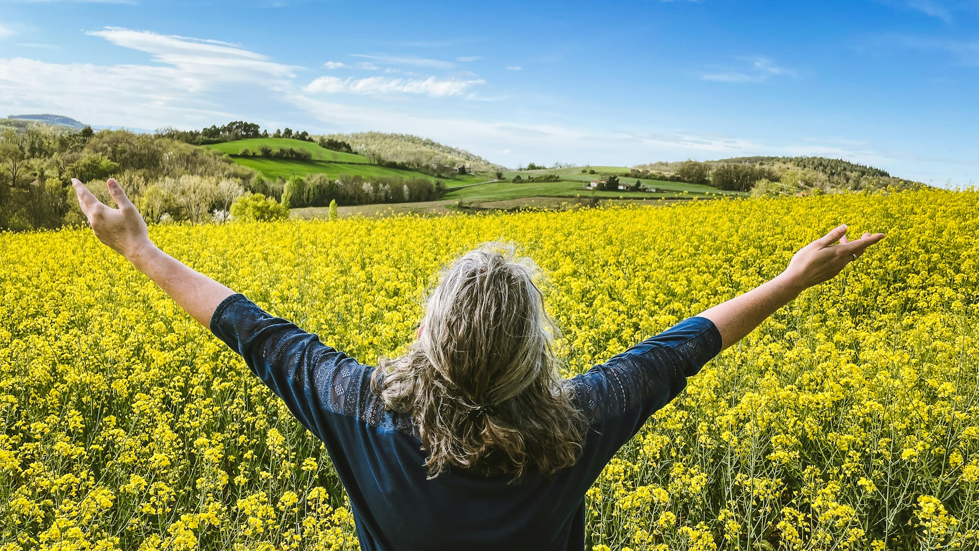 Woman embraces a field of yellow flowers.