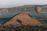 A hot air balloon floats over an ancient pyramid.
