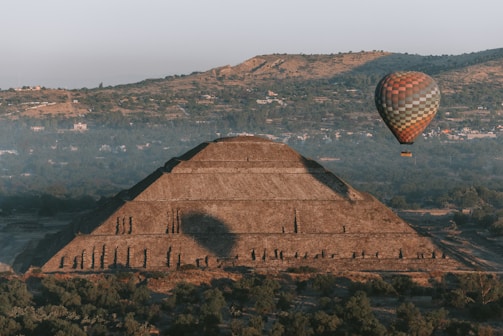 A hot air balloon floats over an ancient pyramid.