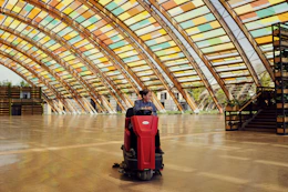 A person uses a floor scrubber inside a building.