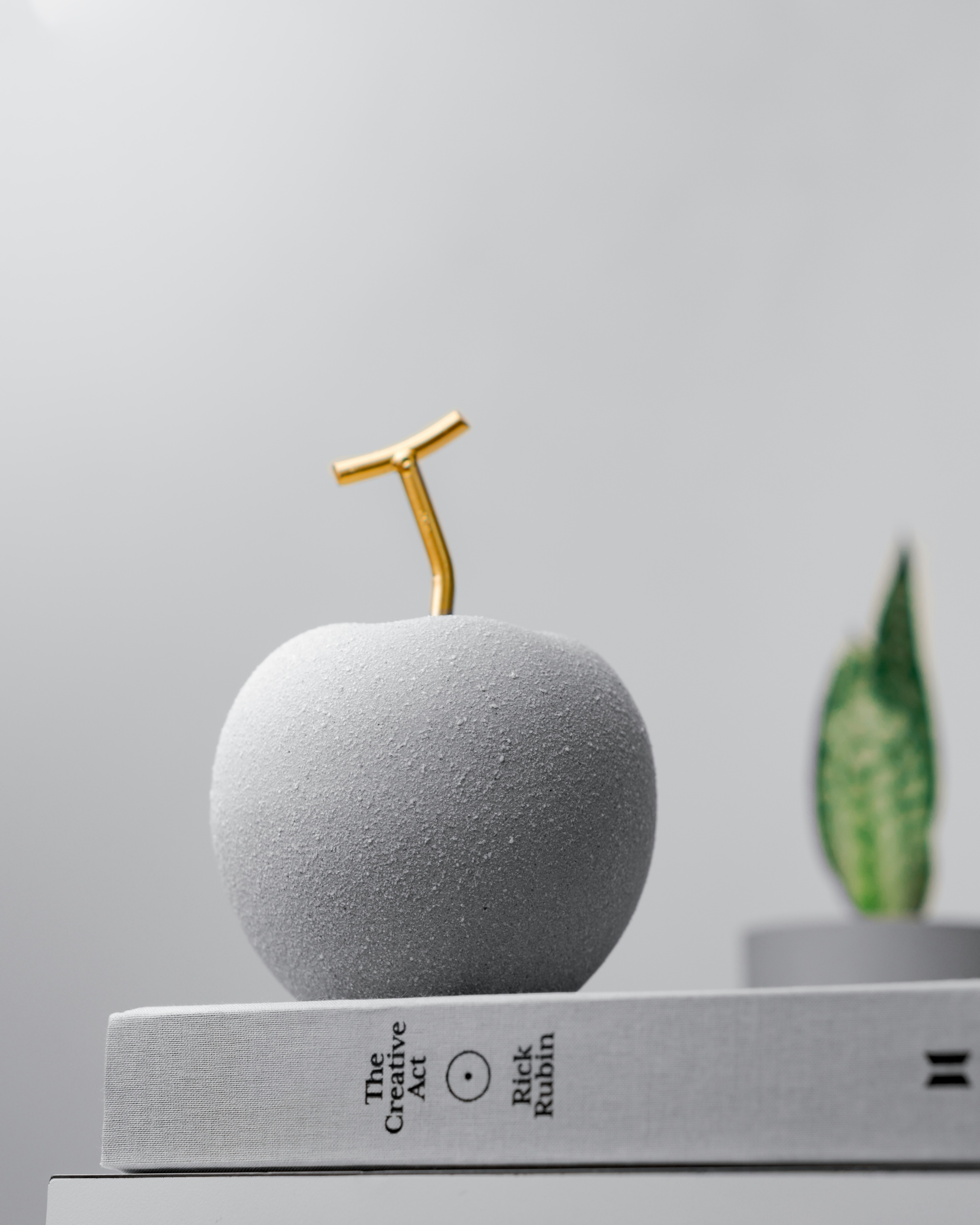 Uma escultura de maçã cinza com uma haste dourada.