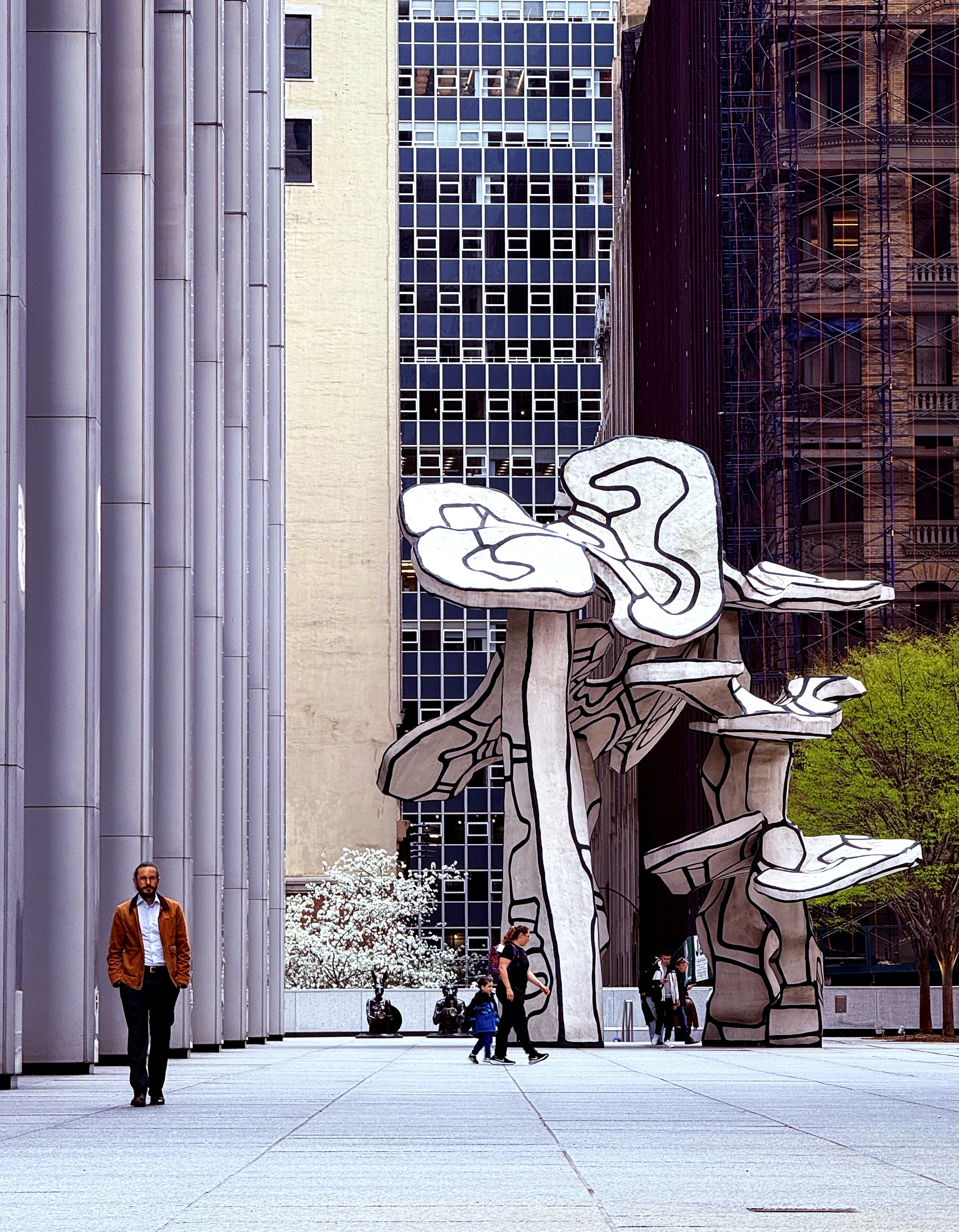 Modern sculpture stands between tall city buildings.